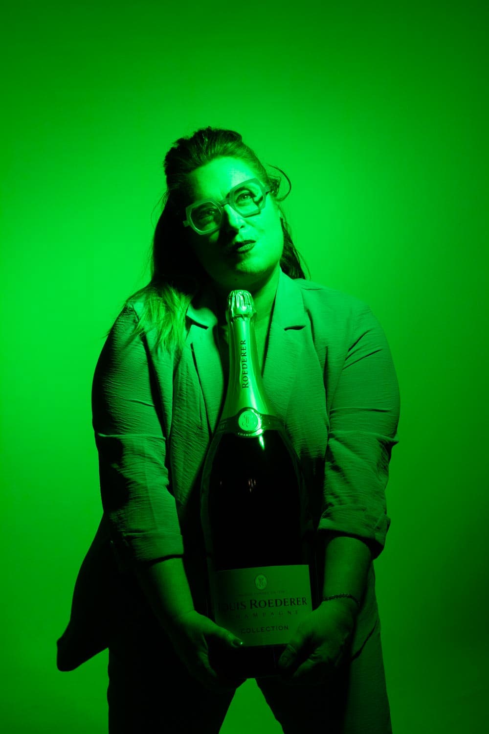 Mélanie Coudert, lunettes signature et champagne sous une lumière verte — Volcanique & Pimenté